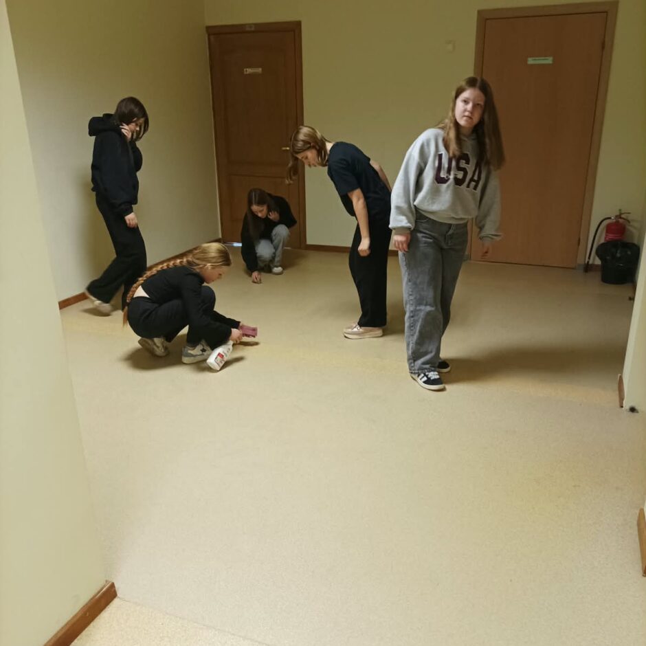 6.a klases skolēni tīra apavu atstātās melnās švīkas no gaiteņa grīdas.