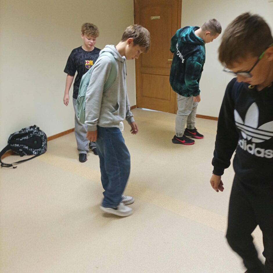 6.a klases skolēni tīra apavu atstātās melnās švīkas no gaiteņa grīdas.