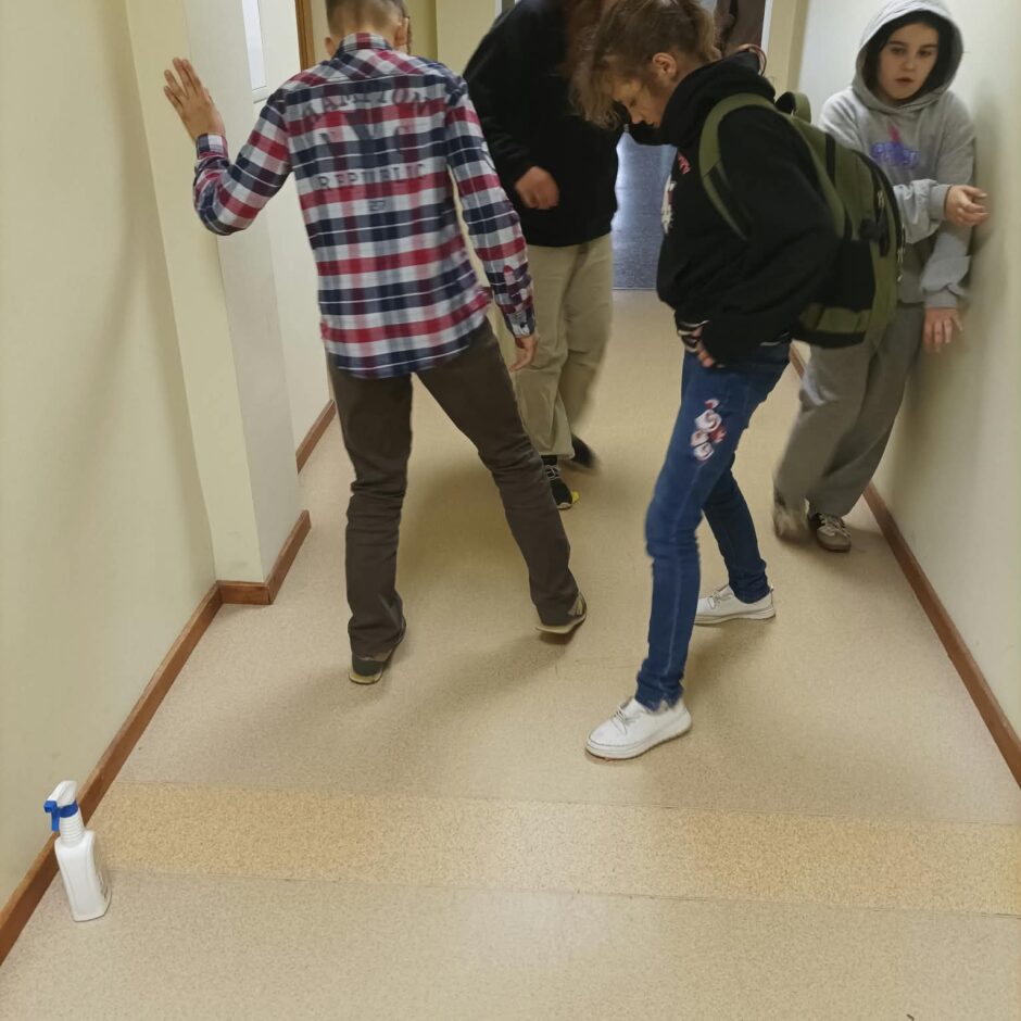 6.a klases skolēni tīra apavu atstātās melnās švīkas no gaiteņa grīdas.